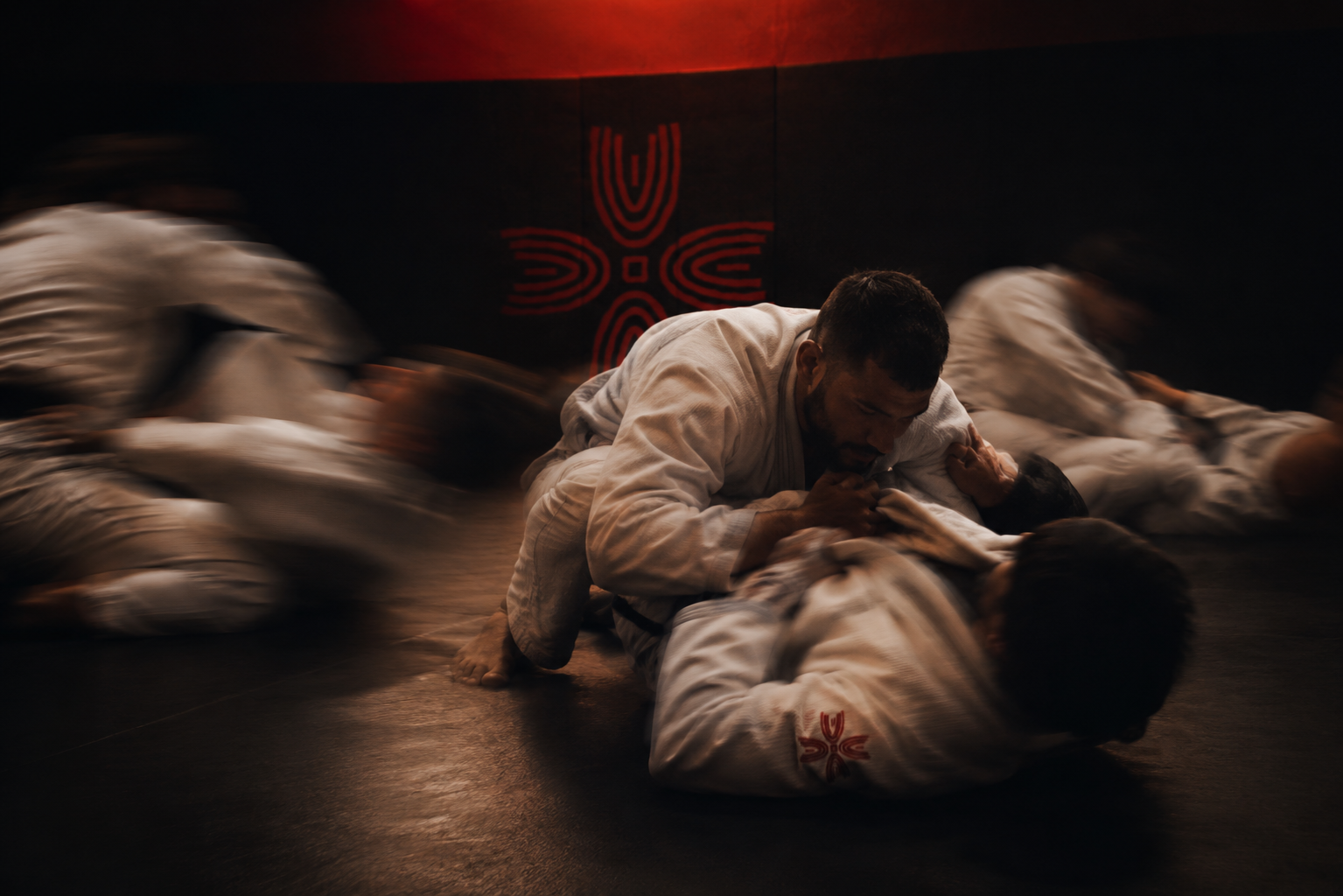 Jiu-Jitsu athletes rolling on the mat with the Mat+ mark on the wall